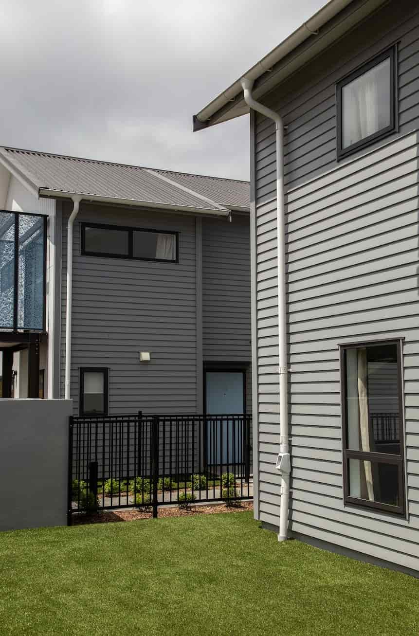 A picturesque grey house with a fence and a beautifully landscaped lawn.