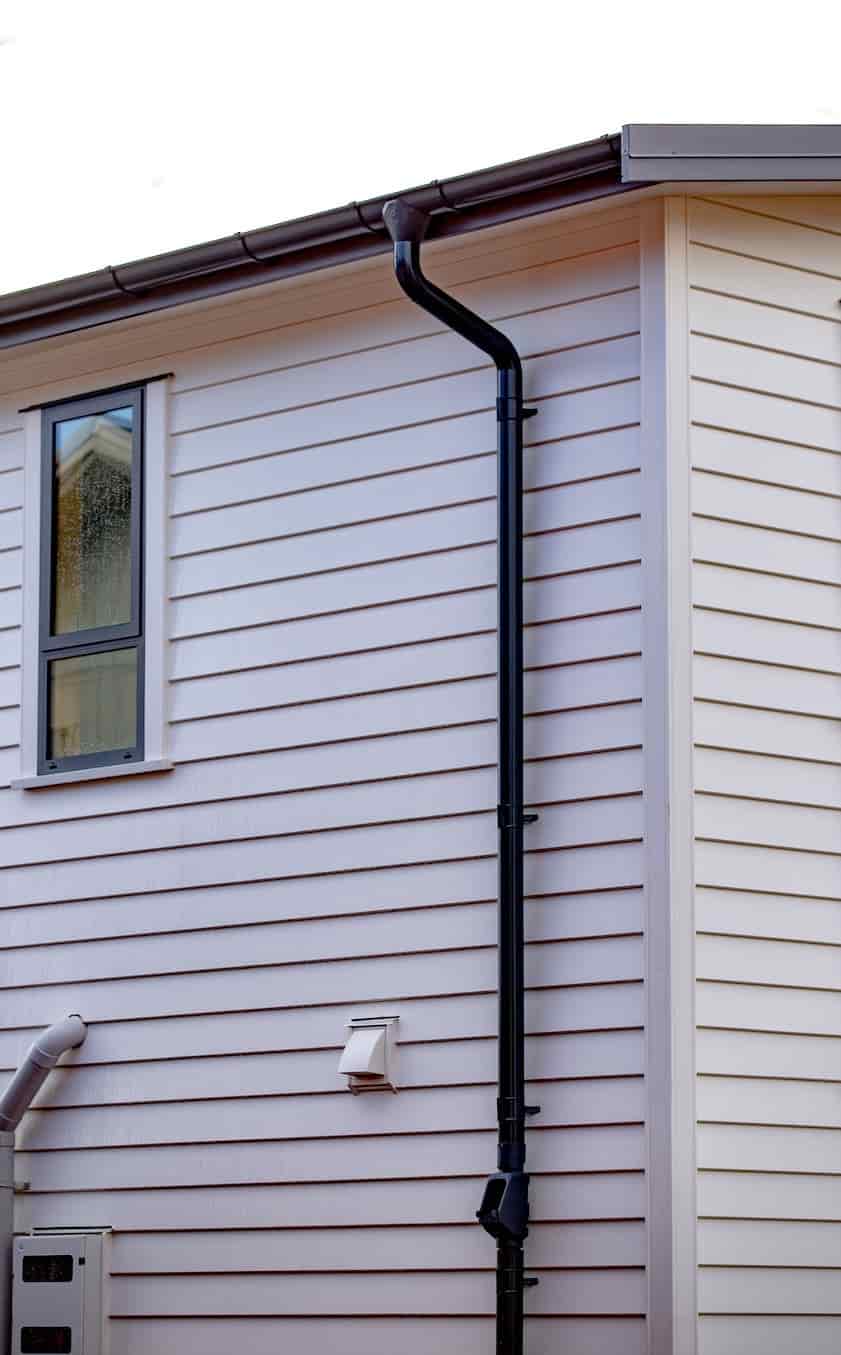 A white house with a black Lindab downpipe on the side.
